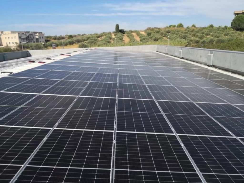A wide rooftop solar panel power plant provided by Eco Green Energy, powering a supermarket in Italy, with fields of an Italian village in the background, as part of a pv installation project to support italy's solar energy industry.